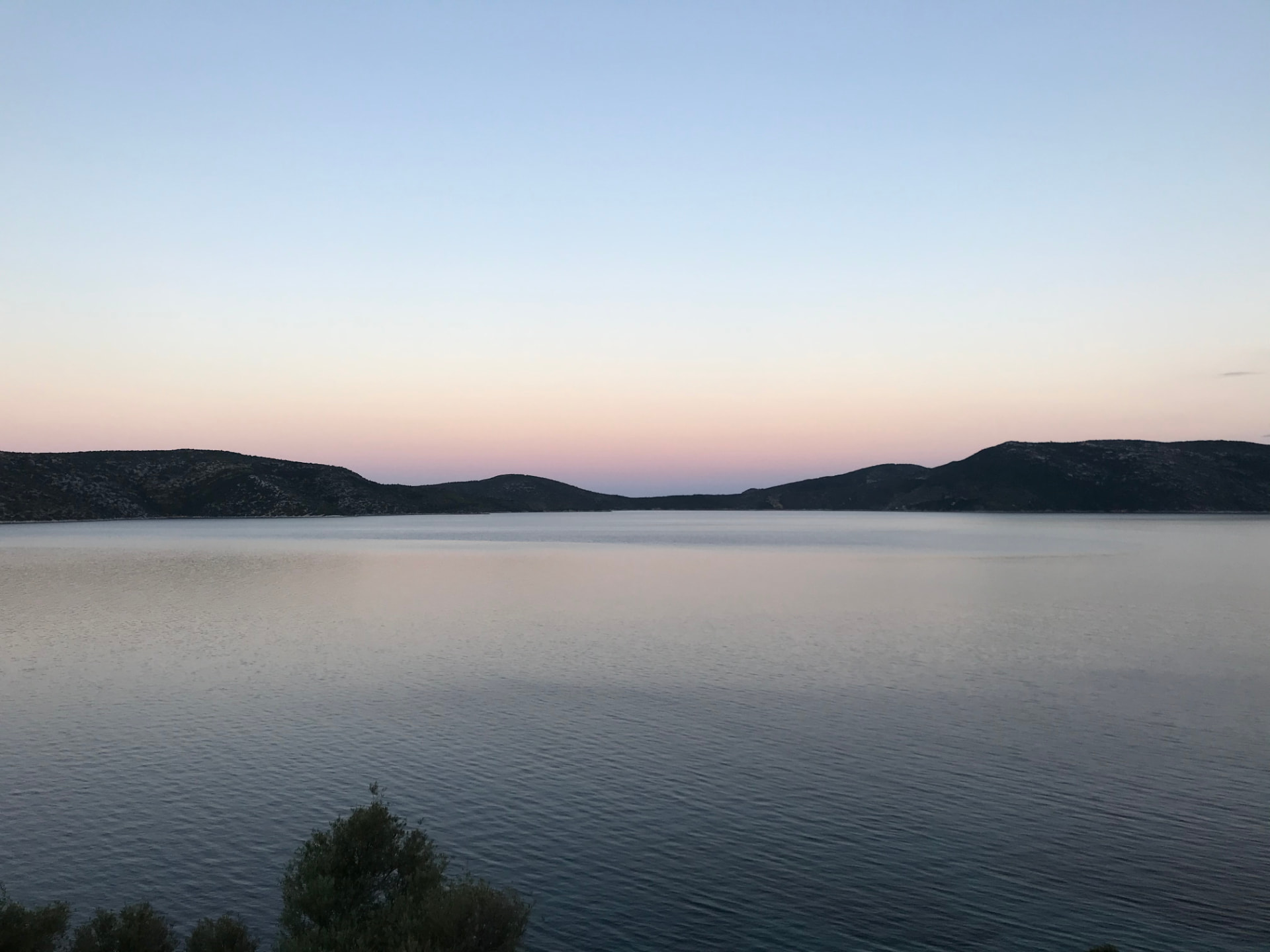 Calm Aegean at dusk with silhouetted hills and a pale pink-blue sky