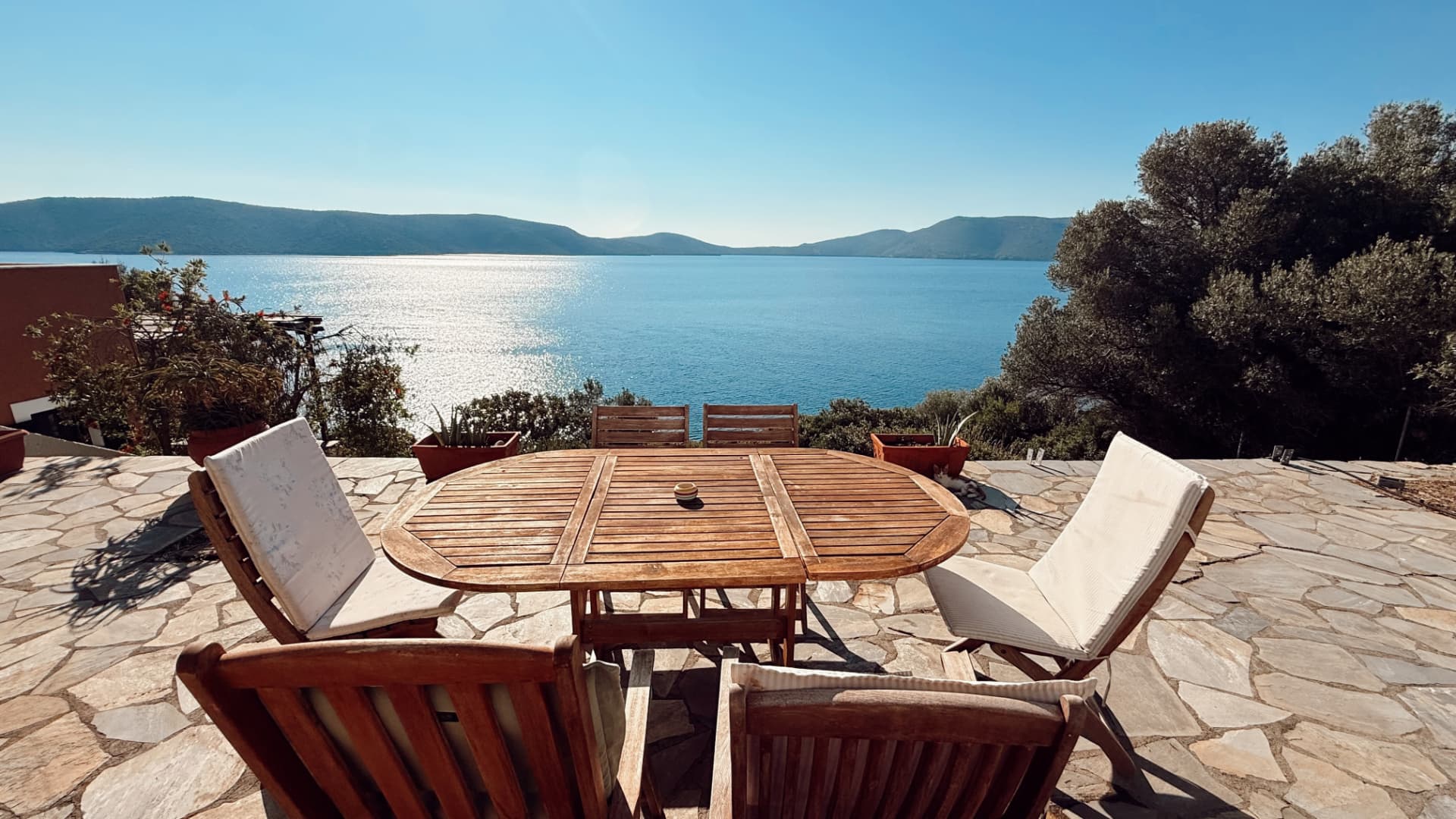 Stone terrace with a wooden dining table and a panoramic sea view