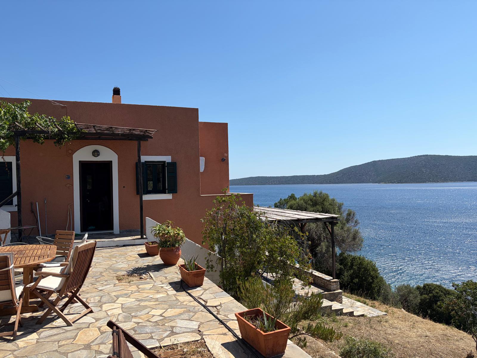 Terracotta villa and stone terrace with potted plants above the blue Aegean